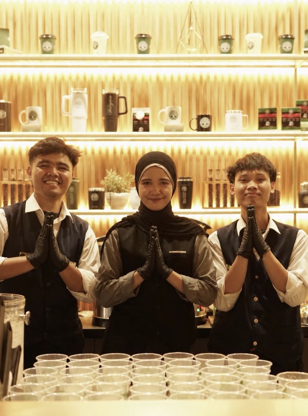 Tim barista Wellgrow berompi dan bersarung tangan hitam memberi salam di depan bar
